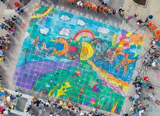 Aerial view of a large sidewalk chalk drawing that says Woodstock with a crowd of spectators