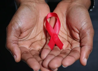 Hands holding a red AIDS advocacy ribbon