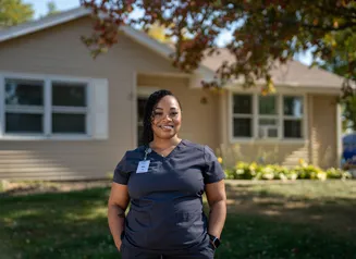 Woman in scrubs standing in front of her home