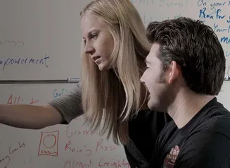People at a computer in front of whiteboard covered with notes