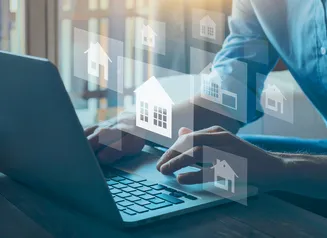 Hands typing on a laptop with housing icons floating in the air