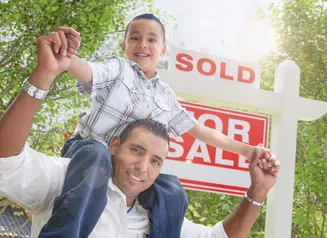 Boy on a man's shoulders in front of a SOLD sign