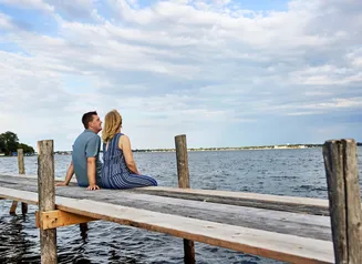 Man and woman sitting on dock looking out at a lake