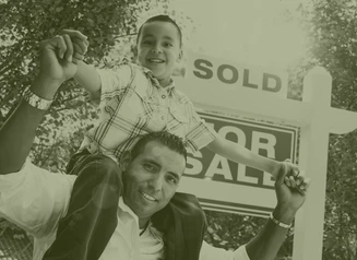 Boy sitting on dad's shoulders in front of For Sale/Sold sign