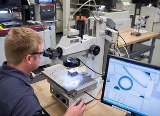 Man looking into a microscope while details show on the monitor of the computer next to him