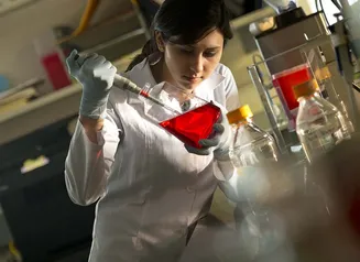 Scientist working with a vial of red liquid in a lab
