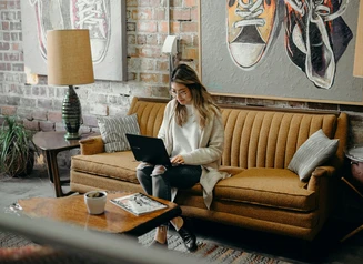 Woman sitting on tan couch, working on laptop