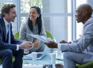 Three businesspeople sitting in green chairs at a low glass table 