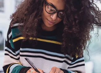 Woman in striped sweater and wearing glasses writing in a notebook