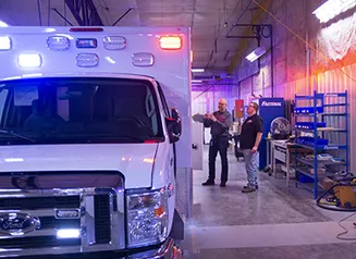 Two men standing next to a white ambulance in a garage setting