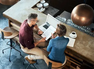 Two people sitting with a laptop and coffees working together at a counter