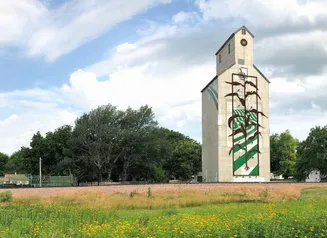 White milk carton-shaped grain elevator with an illustration of green field stripes and a brown corn stalk