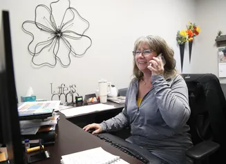 Woman with a cellphone at her ear sitting at a computer in an office setting