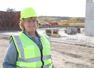 A woman in a neon yellow hard hat and vest standing in front of a construction site
