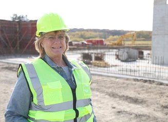 A woman in a neon yellow hard hat and vest standing in front of a construction site