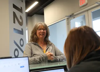 A woman standing in front of a reception desk with 121% on the wall behind her
