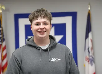 Young man in a hooded sweatshirt standing between Iowa and American flags