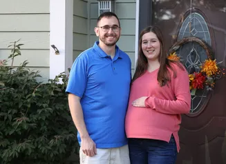 A man and a pregnant woman outside their home in front of a decorated door