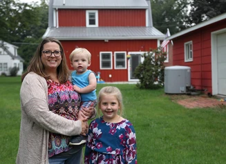 Woman and two children standing in a backyard with a red house behind them