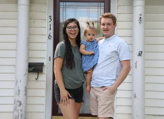 A woman, man and toddler standing in front of their house with columns and a glass door