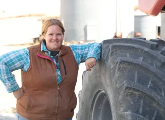 A female farmer standing next to a tractor tire
