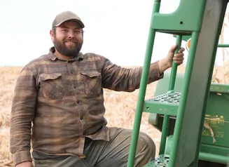 A farmer in a hat standing next to equipment in his field