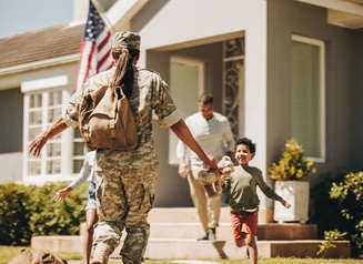 a person in a military uniform running to hug people in front of a home