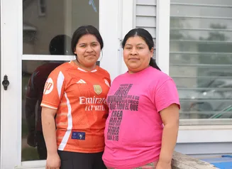 Two women wearing orange and pink standing in front of a house