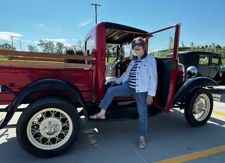 Woman Standing with her leg up on red pick-up truck.