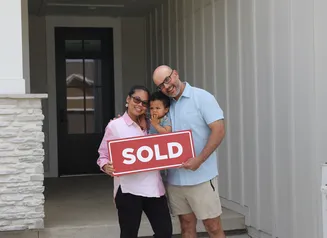 a family standing in front of a home holding a sign that says sold