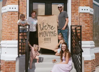 a group of people outside of a storefront holding a sign that says "we're moving in"