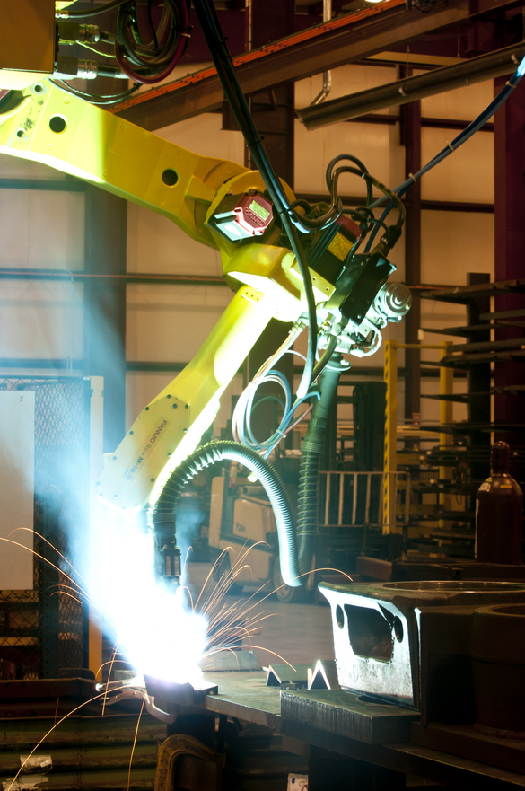 photo of a large, yellow machine welder arm, with a bright light at the welding site.