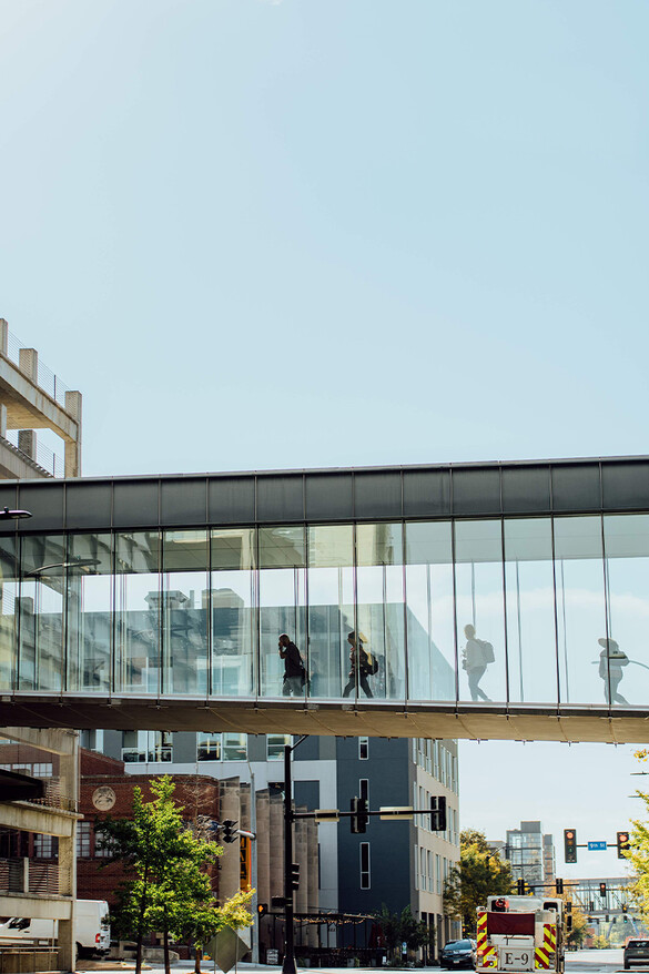 photo of people walking through a glass walled skyway, across a city street from building to building.