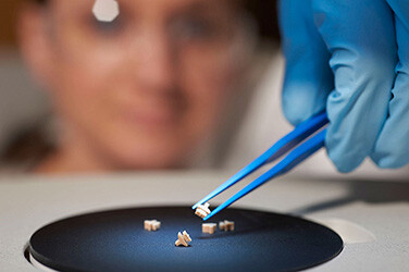 Close up of a gloved hand using tweezers to pick up a very small plastic molded item