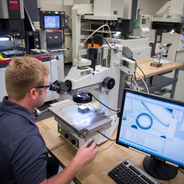 Man looking into a microscope while details show on the monitor of the computer next to him