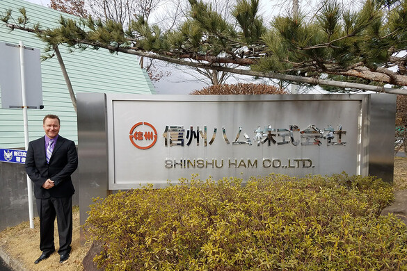 Nick Jones, CEO of Berkwood Farms in front of a sign for Shinshu Ham Co, Ltd written in Japanese and English