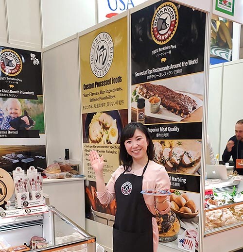 A Japanese woman wearing a Berkwood Farms apron giving out samples in front of signs in Japanese and English