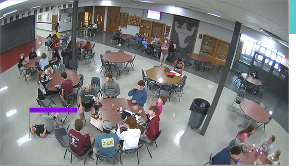 Scene of people sitting at tables with someone lying on the floor and a surveillance indicator showing them on the floor
