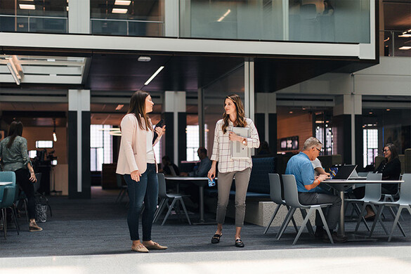 Two women talking while people work at tables in the background