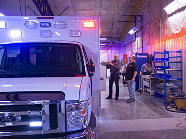 Two men standing next to a white ambulance in a garage setting