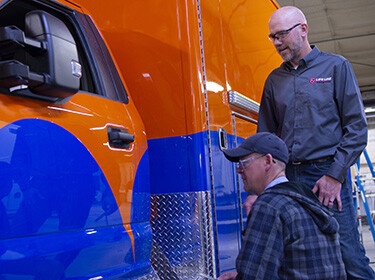 Two men standing next to a blue and orange ambulance