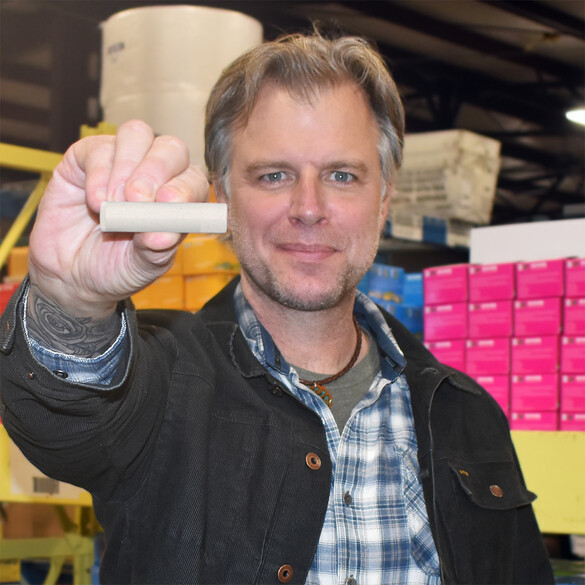 Steve Shriver of Eco Lips holding up a tube in the factory with boxes behind him