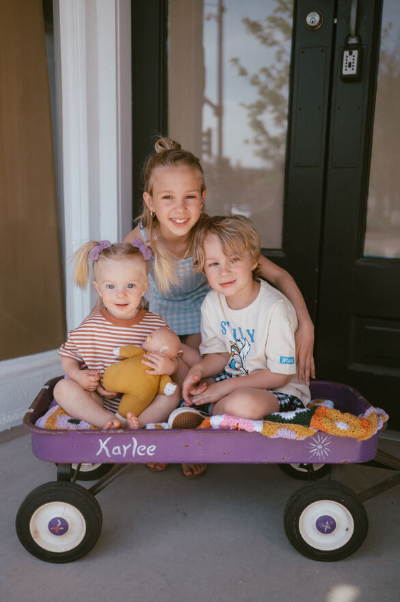 3 kids sitting in a purple wagon