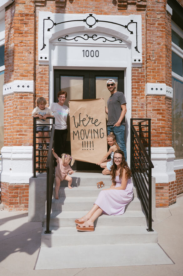 a group of people outside of a storefront holding a sign that says "we're moving in"
